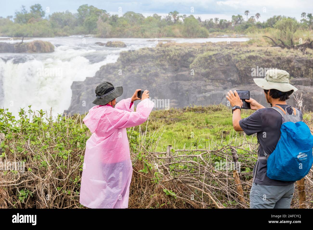 Victoria Falls, Zimbabwe. Two hikers take pictures of the falls. Livingstone Island can be seen in the background. Stock Photo