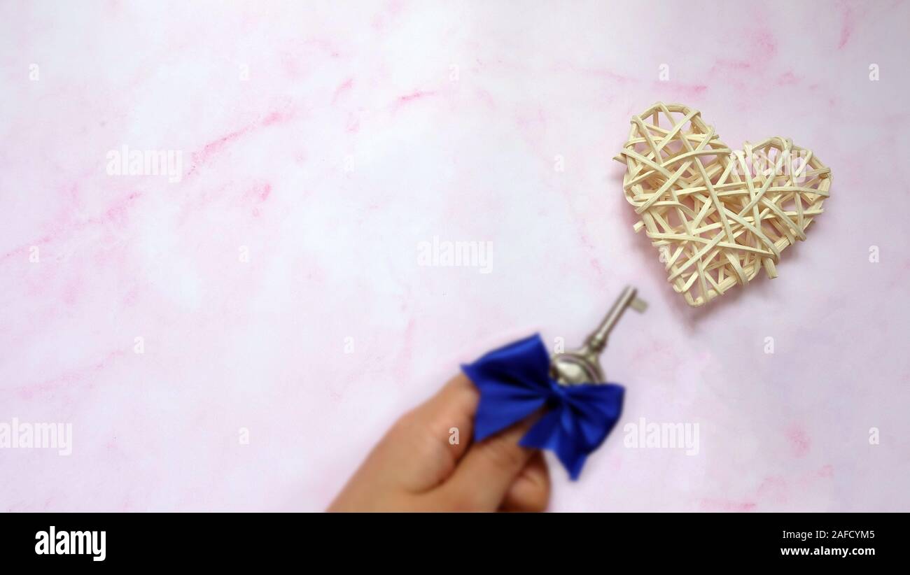 A hand holding a small key tied with a blue ribbon, near a rattan woven ...