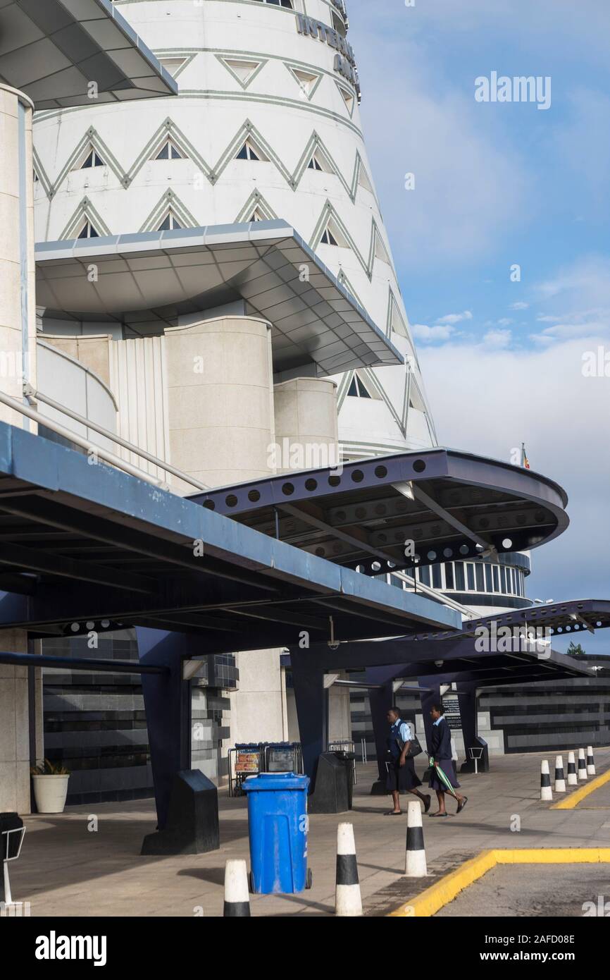 Harare, Zimbabwe. Two flight attendants enter the international terminal in the Robert Gabriel Muabe international airport. The control tower of  the airport,above the terminal entrance, is designed to resemble the conical tower the Great Zimbabwe ruin. Stock Photo