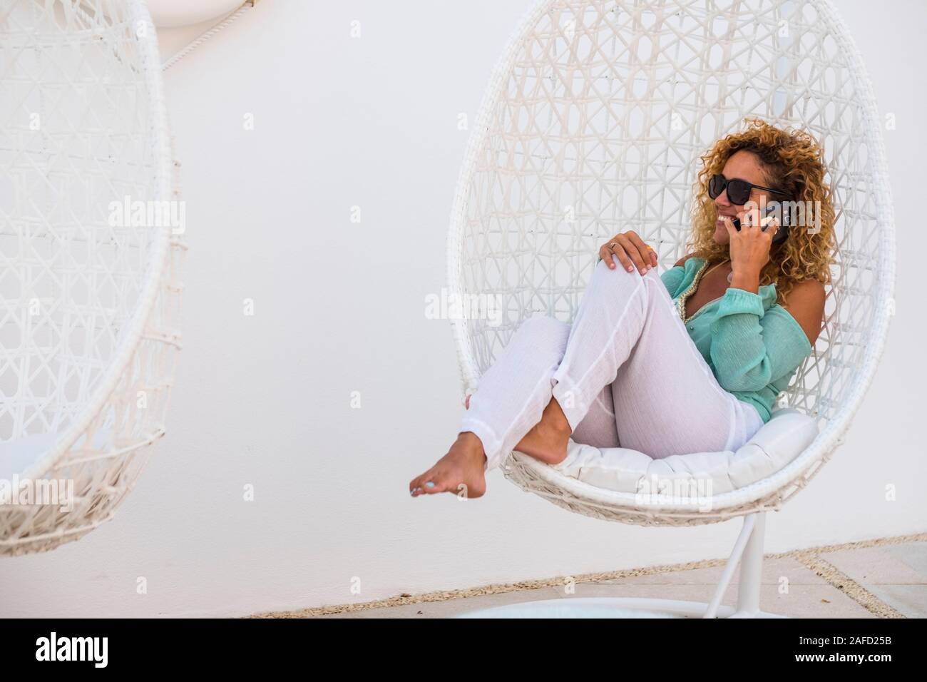 Beautiful happy cheerful caucasian lady speak at the phone in a call while enjoy the white elegant chairs outdoor - luxury rich lifestyle people conce Stock Photo