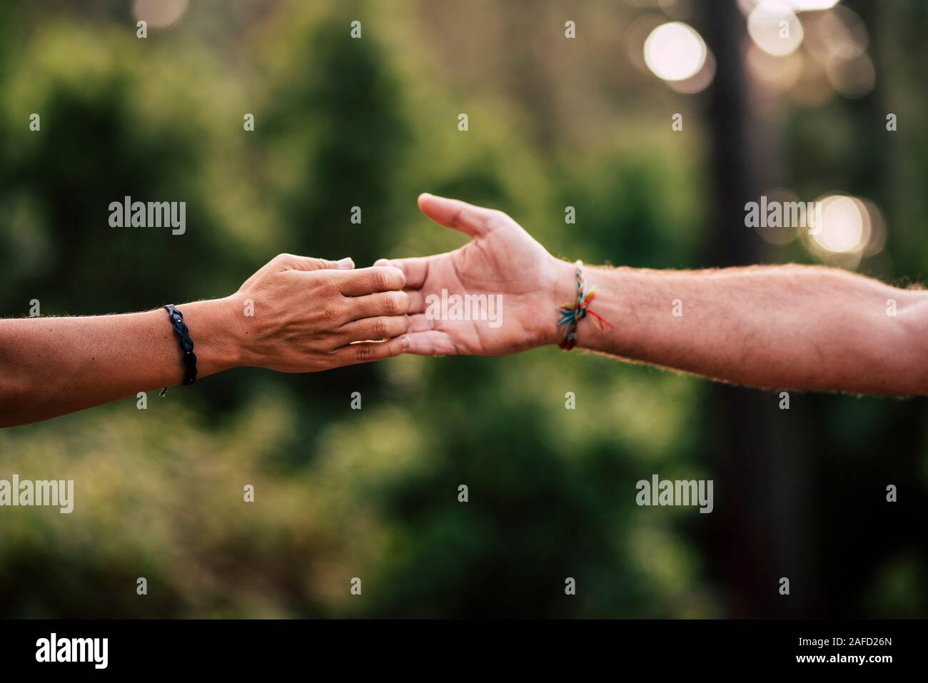 Close up of man and woman caucasian hands touching and holding with love and friendship - unrecognized people and green outdoor nature background - he Stock Photo
