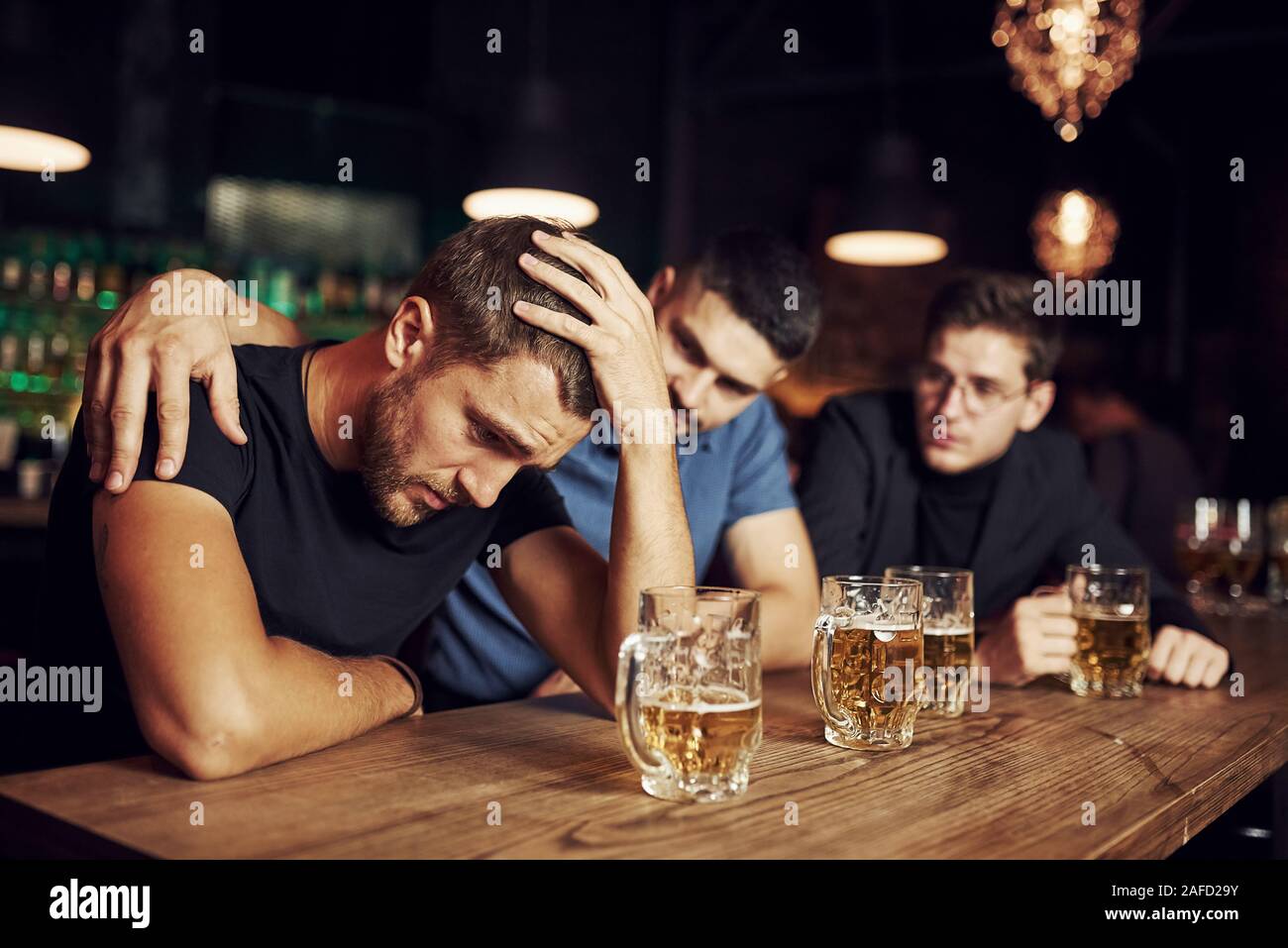 Three male friends in the bar. Supporting sad friend. Unity of people. With beer on the table Stock Photo