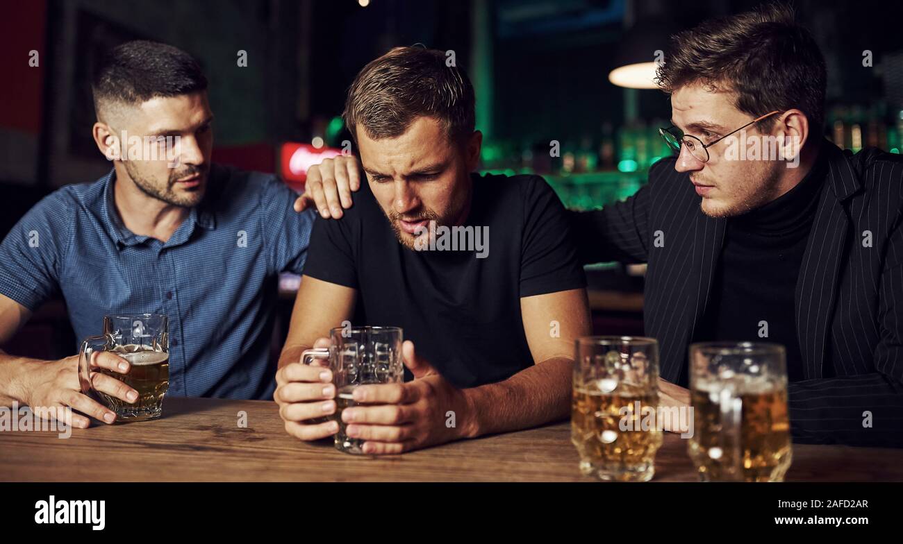 Three male friends in the bar. Supporting sad friend. Unity of people. With beer on the table Stock Photo