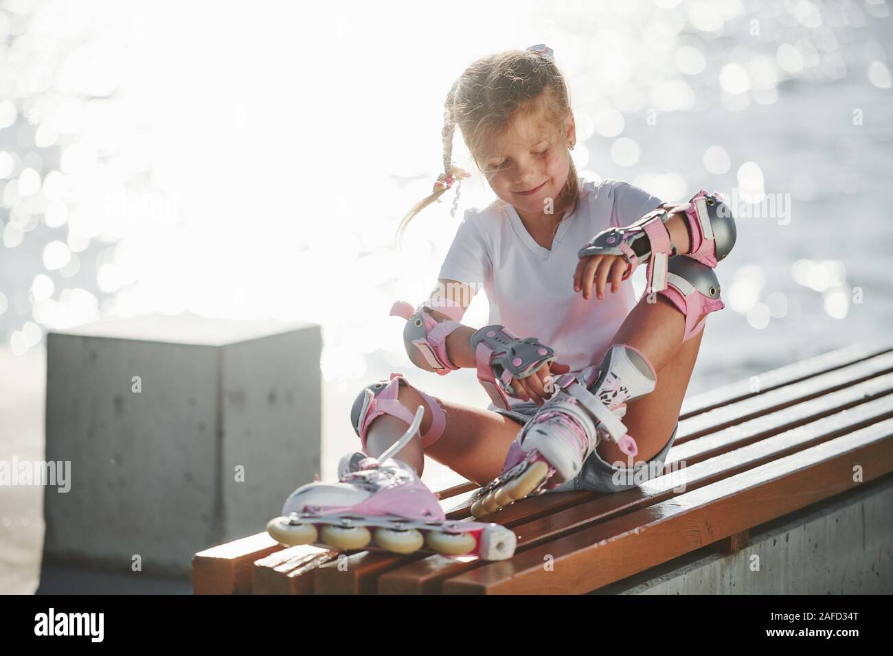 Fixing her skate roller. Cute little girl outdoors near the lake at
