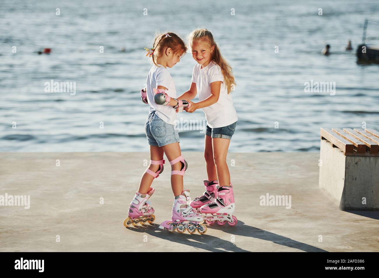 Two kids learning how to ride on roller skates at daytime near the lake