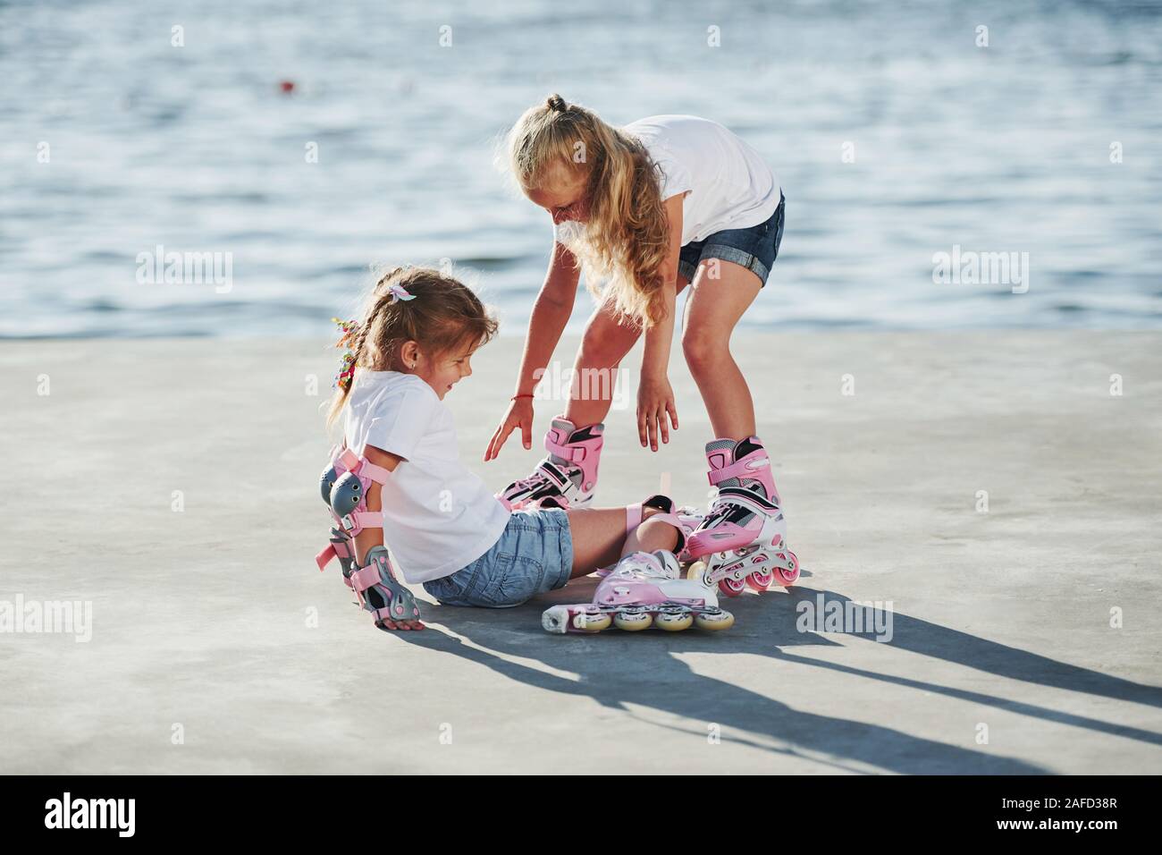 Two kids learning how to ride on roller skates at daytime near the lake