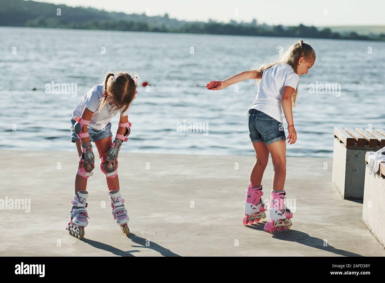 Two kids learning how to ride on roller skates at daytime near the lake