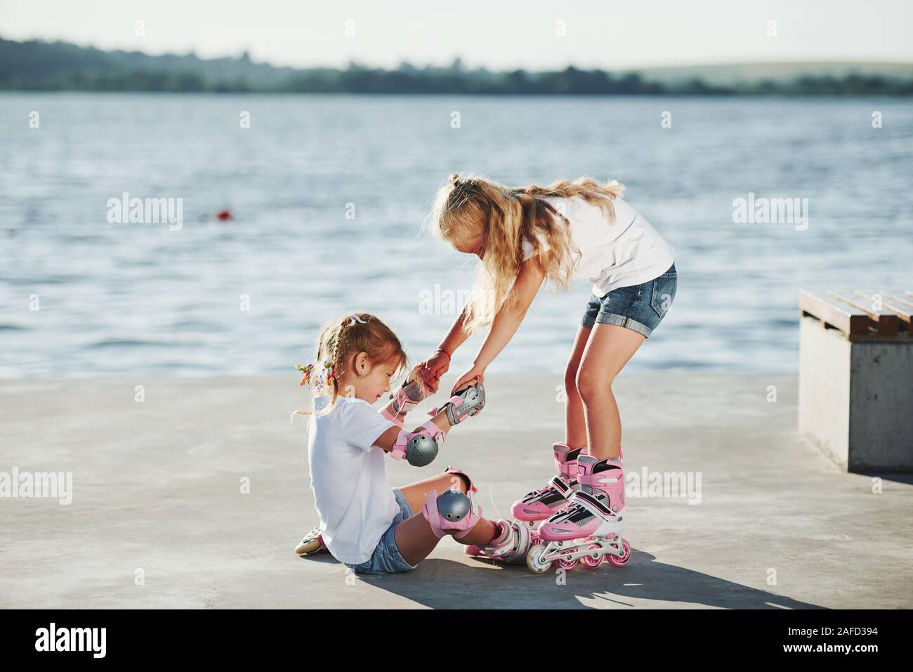 Two kids learning how to ride on roller skates at daytime near the lake