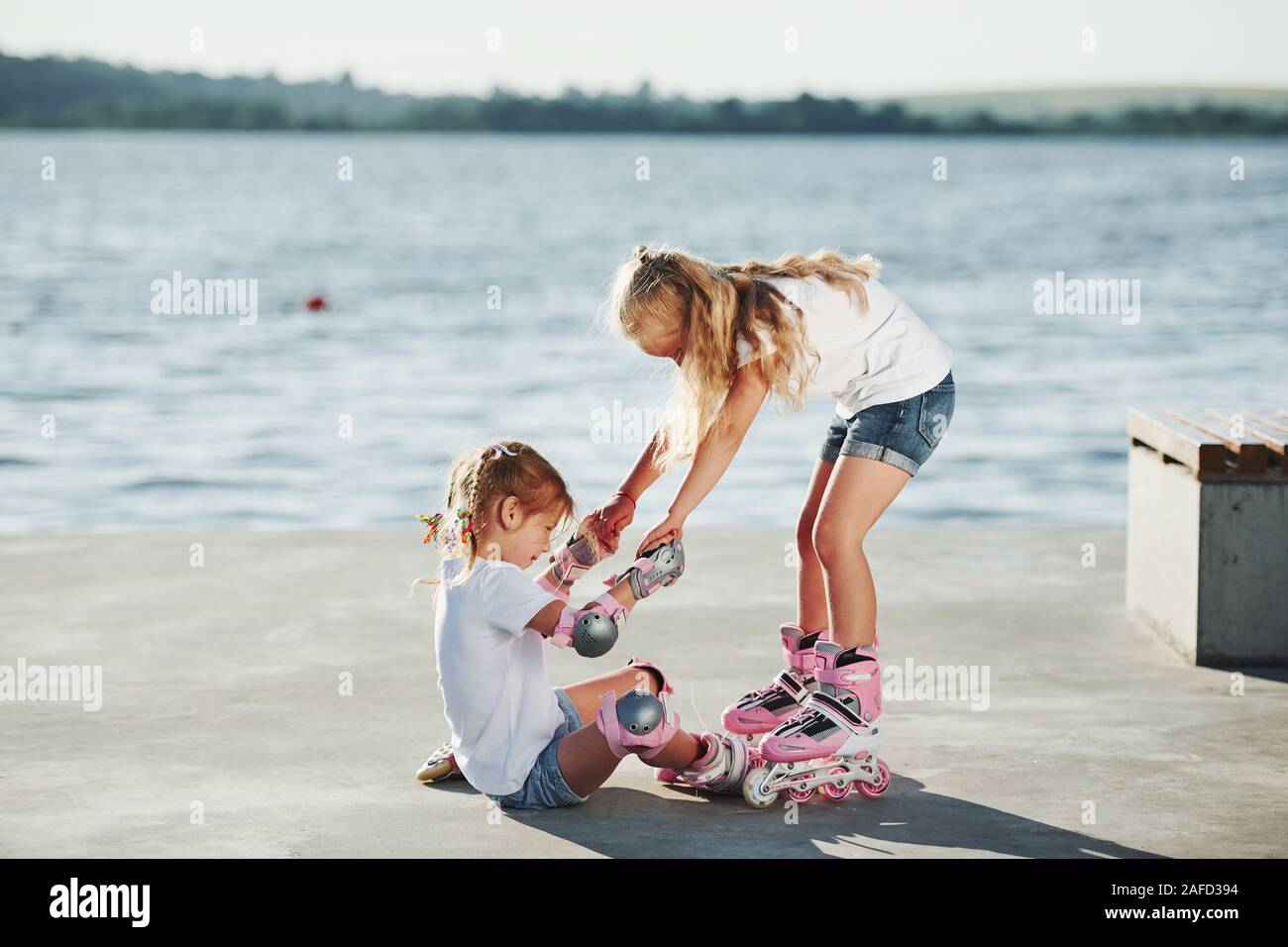 Two kids learning how to ride on roller skates at daytime near the lake Stock Photo