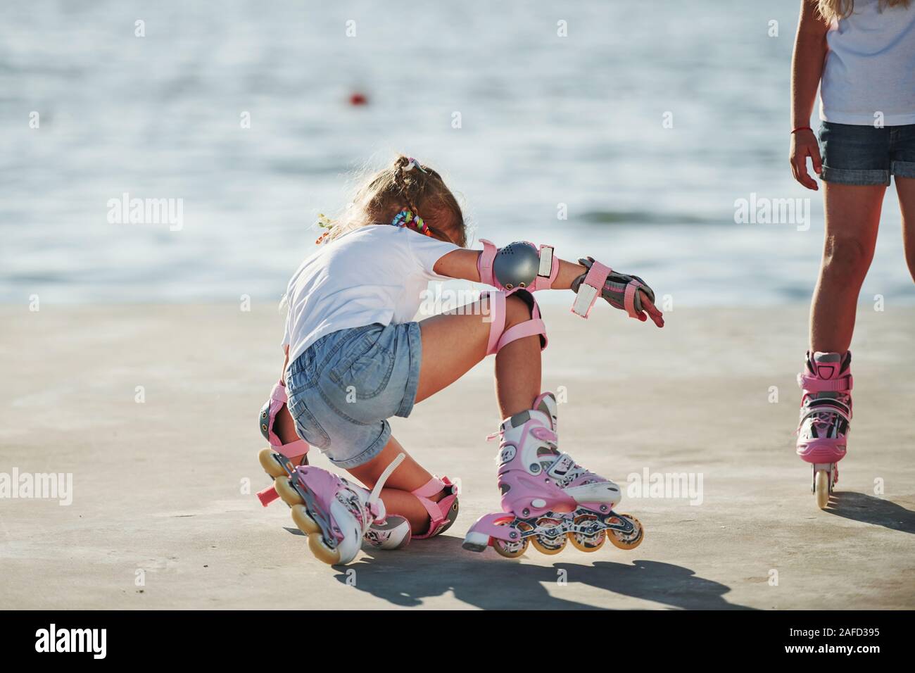 Two kids learning how to ride on roller skates at daytime near the lake Stock Photo