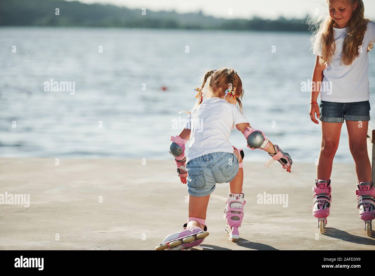 Two kids learning how to ride on roller skates at daytime near the lake
