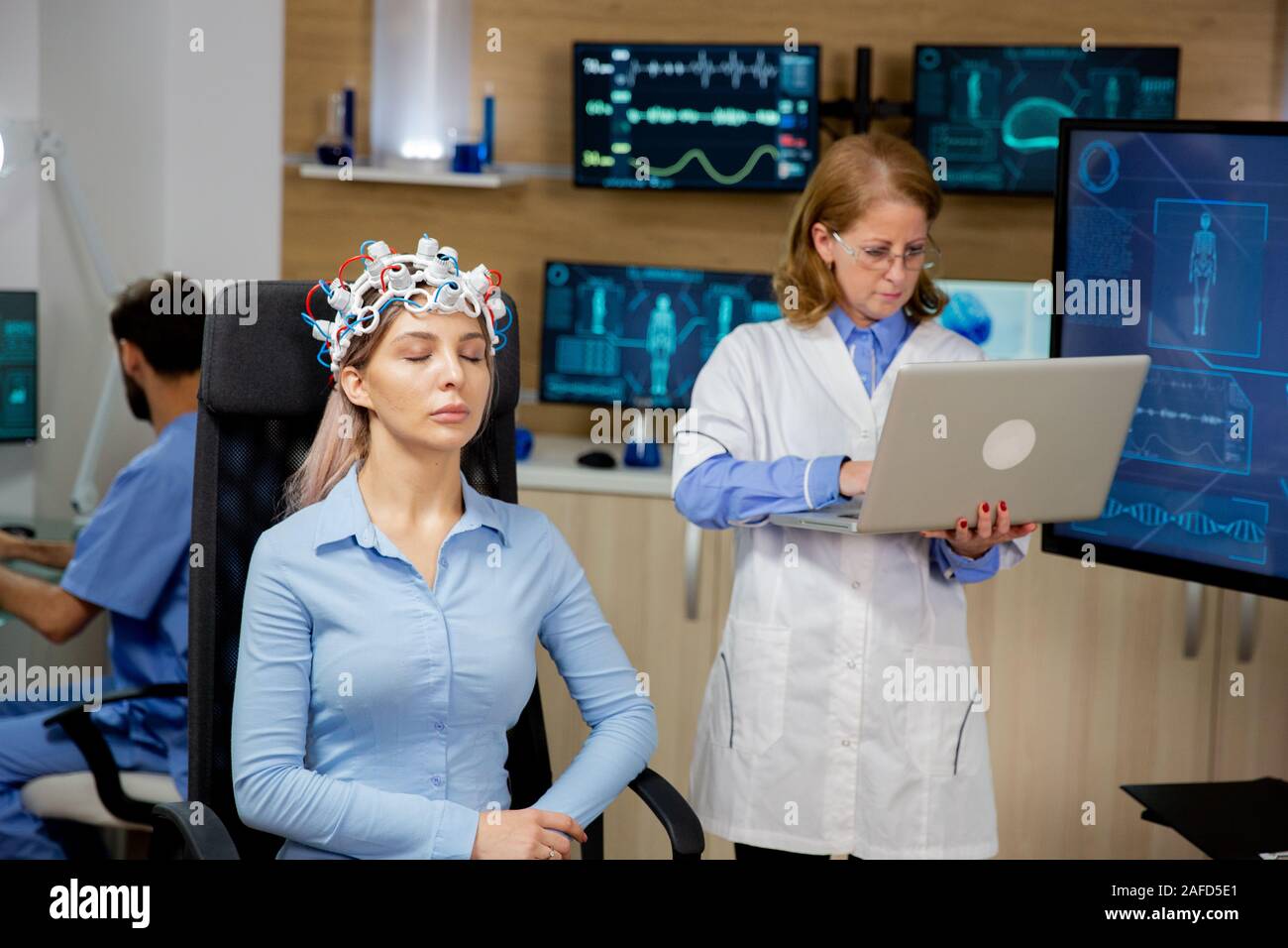 Doctor researching live data on a laptop during a girl's brain scan procedure. Brain waves scanning helmet Stock Photo