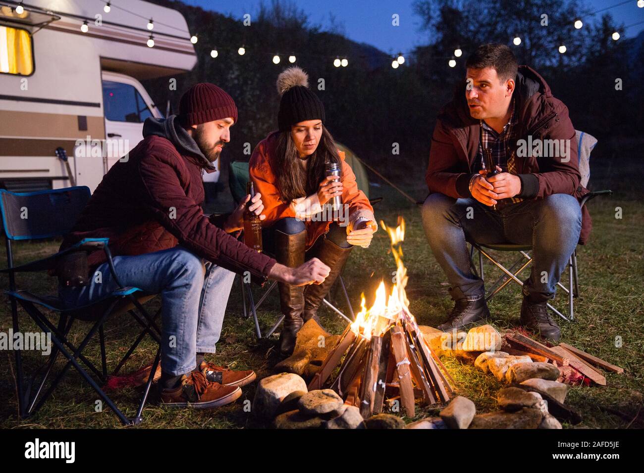 Campers relaxing together around camp fire and drinking beer. Retro