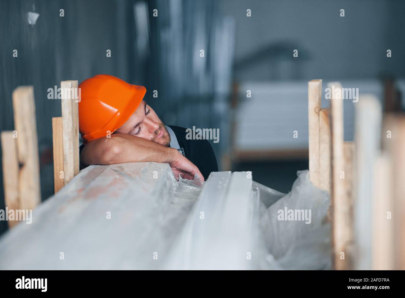 Sleeping on a job. Taking a break. Industrial worker indoors in factory. Young technician with orange hard hat Stock Photo