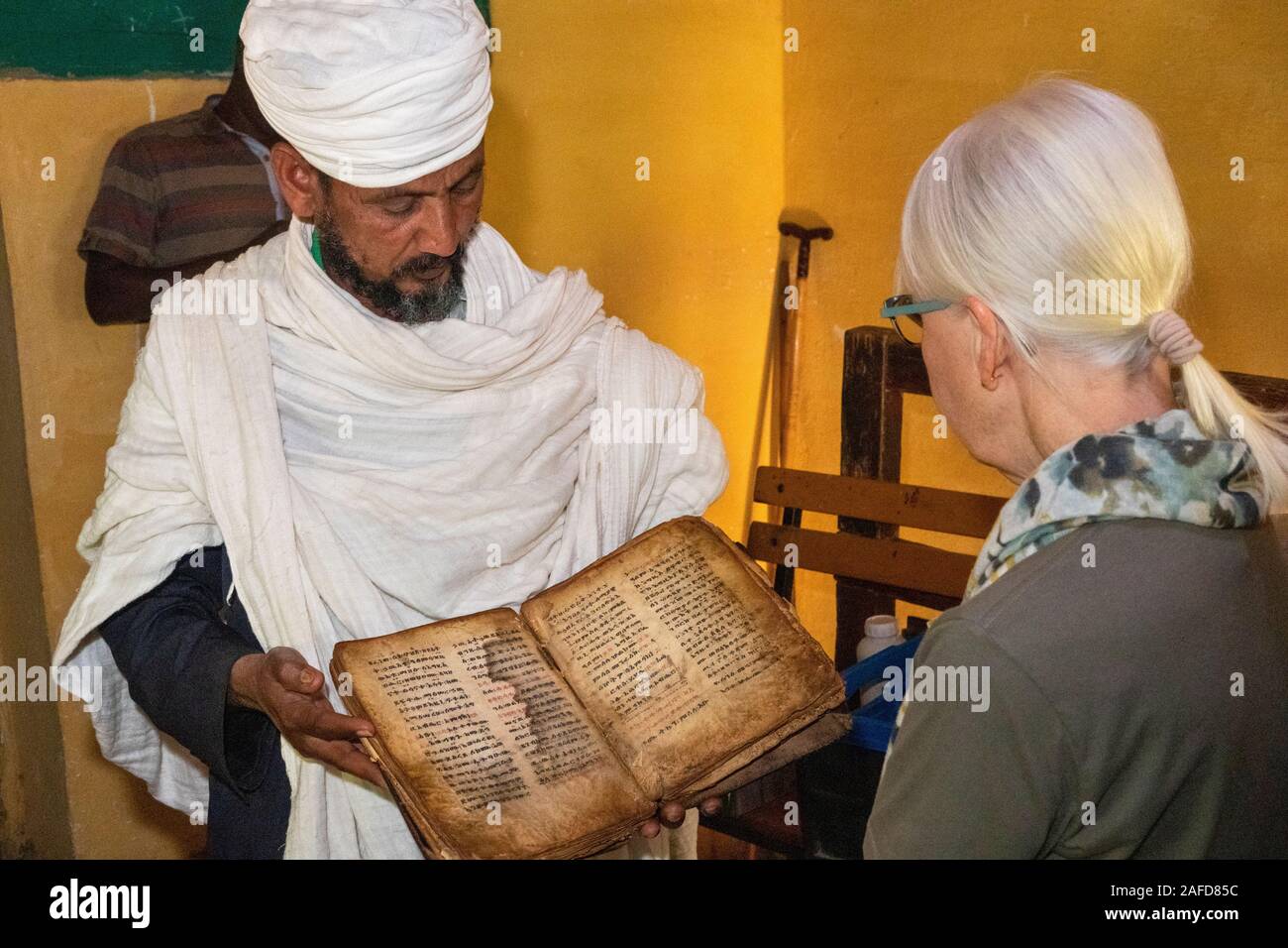 Ethiopia, Tigray, Adwa, Yeha, priest showing senior female tourist ancient manuscript in Ge'ez script Stock Photo