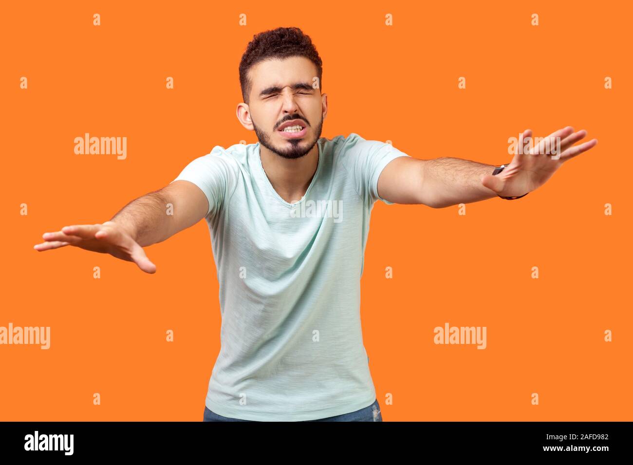 Blindness! Portrait of disoriented brunette man with beard in casual white t-shirt walking with eyes closed and holding out his hands to find road. in Stock Photo