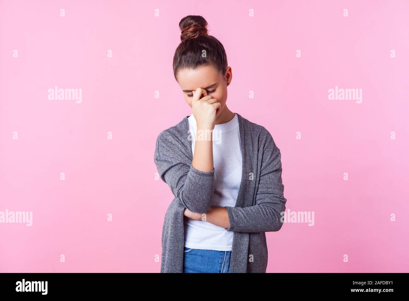 Portrait of upset teenage girl with bun hairstyle in casual clothes hiding face in hand