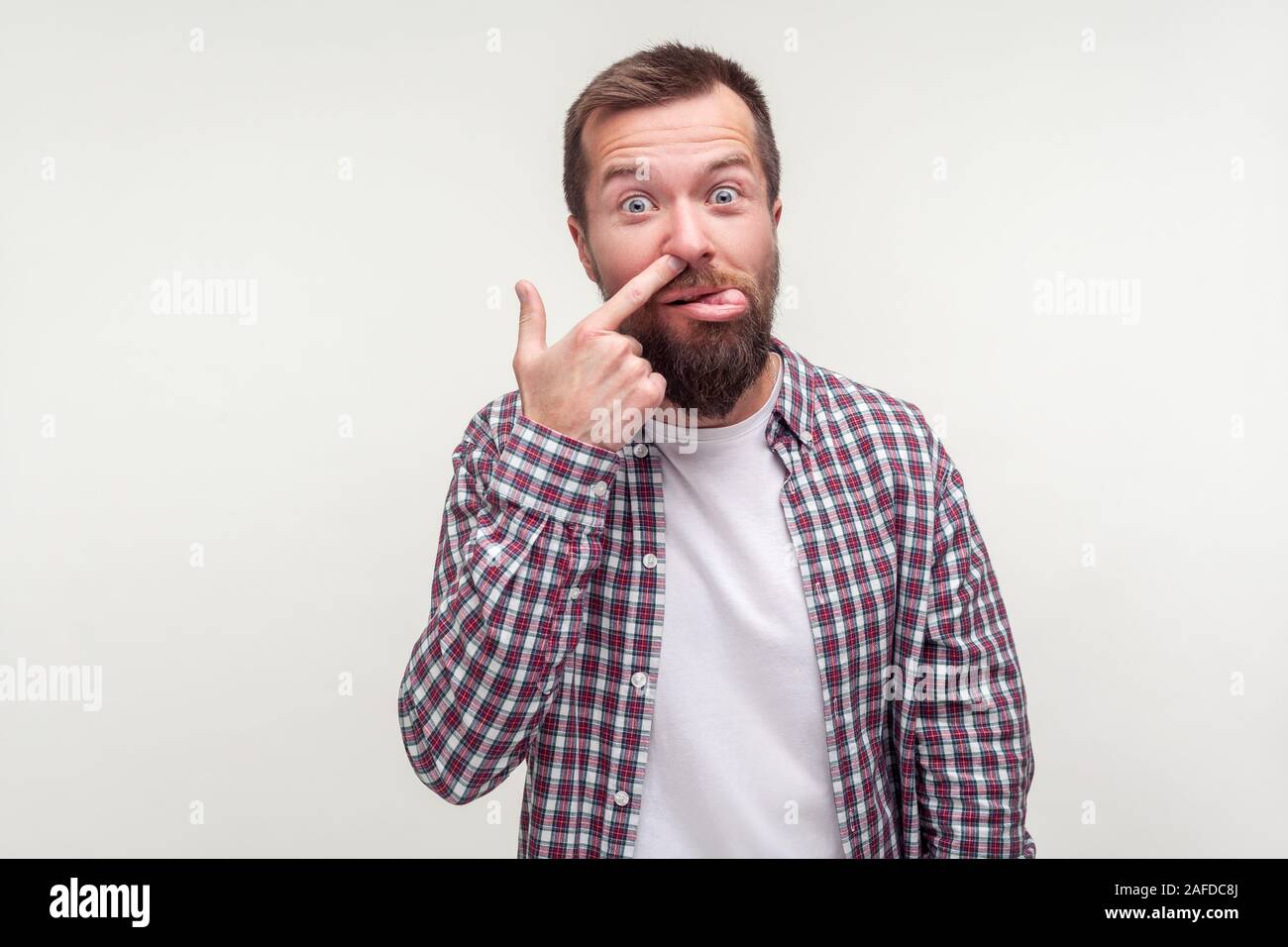 Portrait of funny silly bearded man in casual plaid shirt picking nose and showing tongue with comical stupid face, adult with bad manners, misconduct Stock Photo