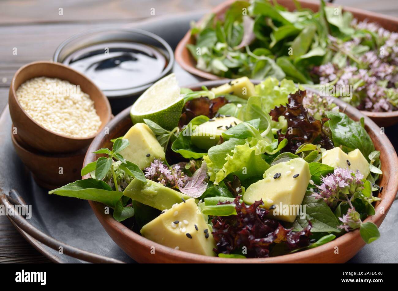 Clay dish with salad of avocado, green and violet lettuce, lamb's lettuce and oregano flowers on slate stone tray with soy sauce lime and sesame aside Stock Photo
