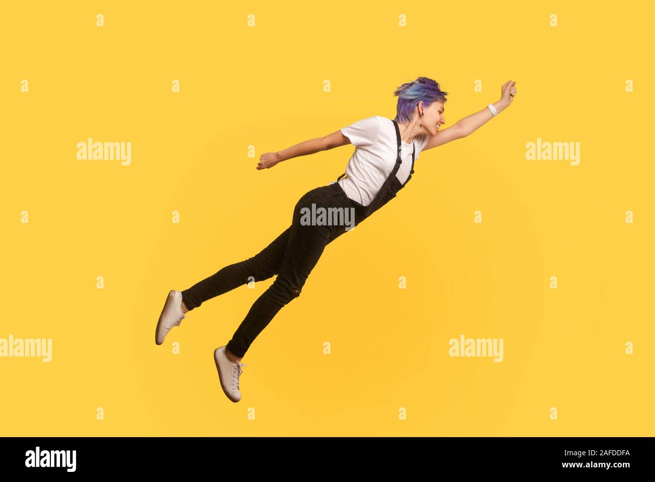 Superman. Portrait of enthusiastic ambitious hipster girl with violet short hair in denim overalls flying like superhero in air, feeling free, strivin Stock Photo