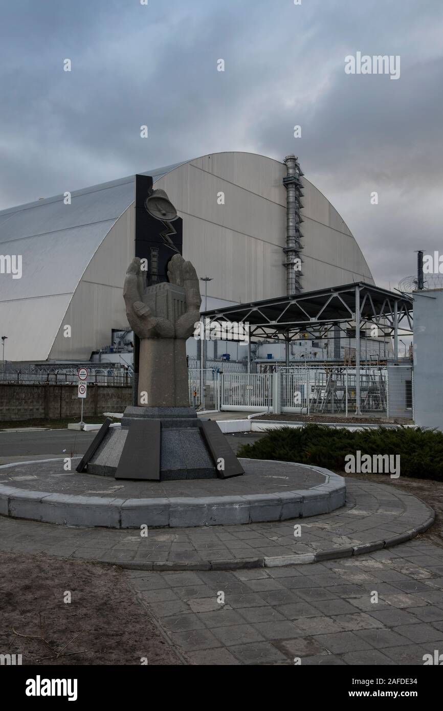 The monument to the Chernobyl liquidators (which once constructed the old sarcophagos) in front of the New Safe Confinement in its final position. The new shelter is a structure built to confine the remains of the number 4 reactor unit at the Chernobyl Nuclear Power Plant, in Ukraine, which was destroyed during the Chernobyl disaster in 1986.Chernobyl nuclear power plant, Chernobyl, Ivankiv Raion, Kiev Oblast, Ukraine, Europe Stock Photo