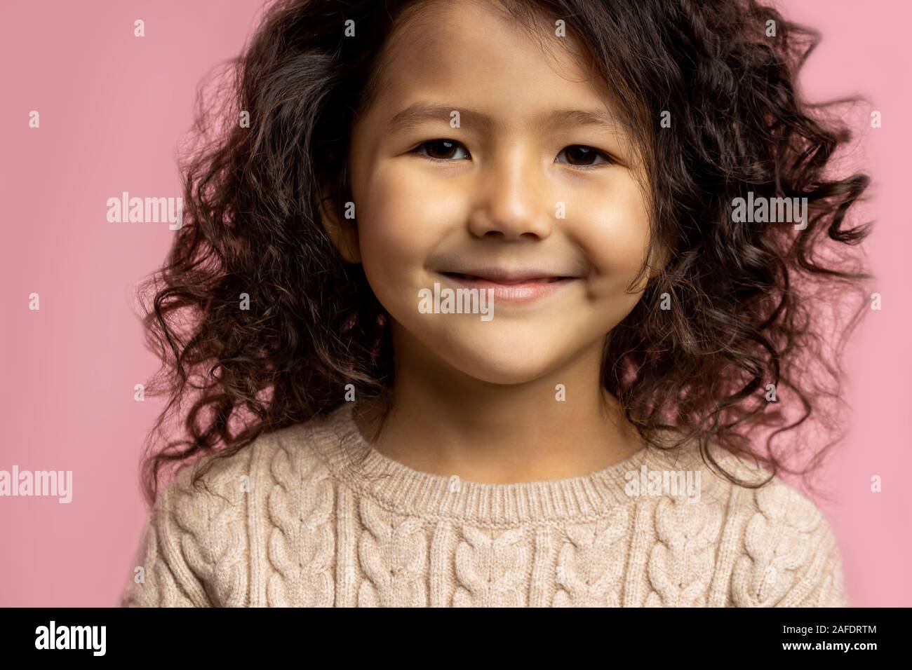 Close up cropped studio portrait of little kid girl 5 . with dark curly  hair, brown skin, charming smile, brown eyes, wearing beige sweater, smilin  Stock Photo - Alamy
