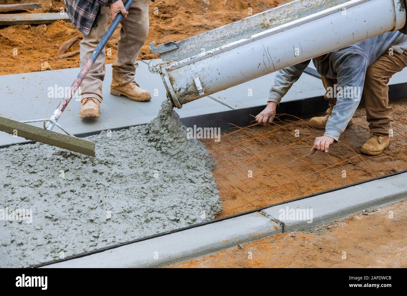 Mixer truck operator pouring cement concrete casting on reinforcing metal bars of sidewalk Stock Photo