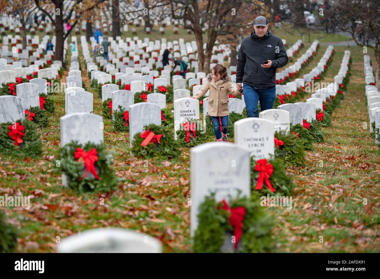 Arlington, United States of America. 14 December, 2019. Family members walk past gravesites of fallen service members marked by wreaths during the 28th Wreaths Across America Day at Arlington National Cemetery December 14, 2019 in Arlington, Virginia. More than 38,000 volunteers place wreaths at every gravesite at Arlington National Cemetery and other sites around the nation.  Credit: Elizabeth Fraser/DOD/Alamy Live News Stock Photo