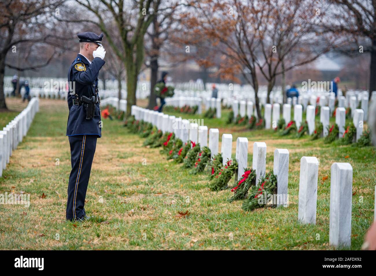 Arlington, United States of America. 14 December, 2019. A State Police volunteer salutes after placing a wreath on gravesites of fallen service members during the 28th Wreaths Across America Day at Arlington National Cemetery December 14, 2019 in Arlington, Virginia. More than 38,000 volunteers place wreaths at every gravesite at Arlington National Cemetery and other sites around the nation.  Credit: Elizabeth Fraser/DOD/Alamy Live News Stock Photo