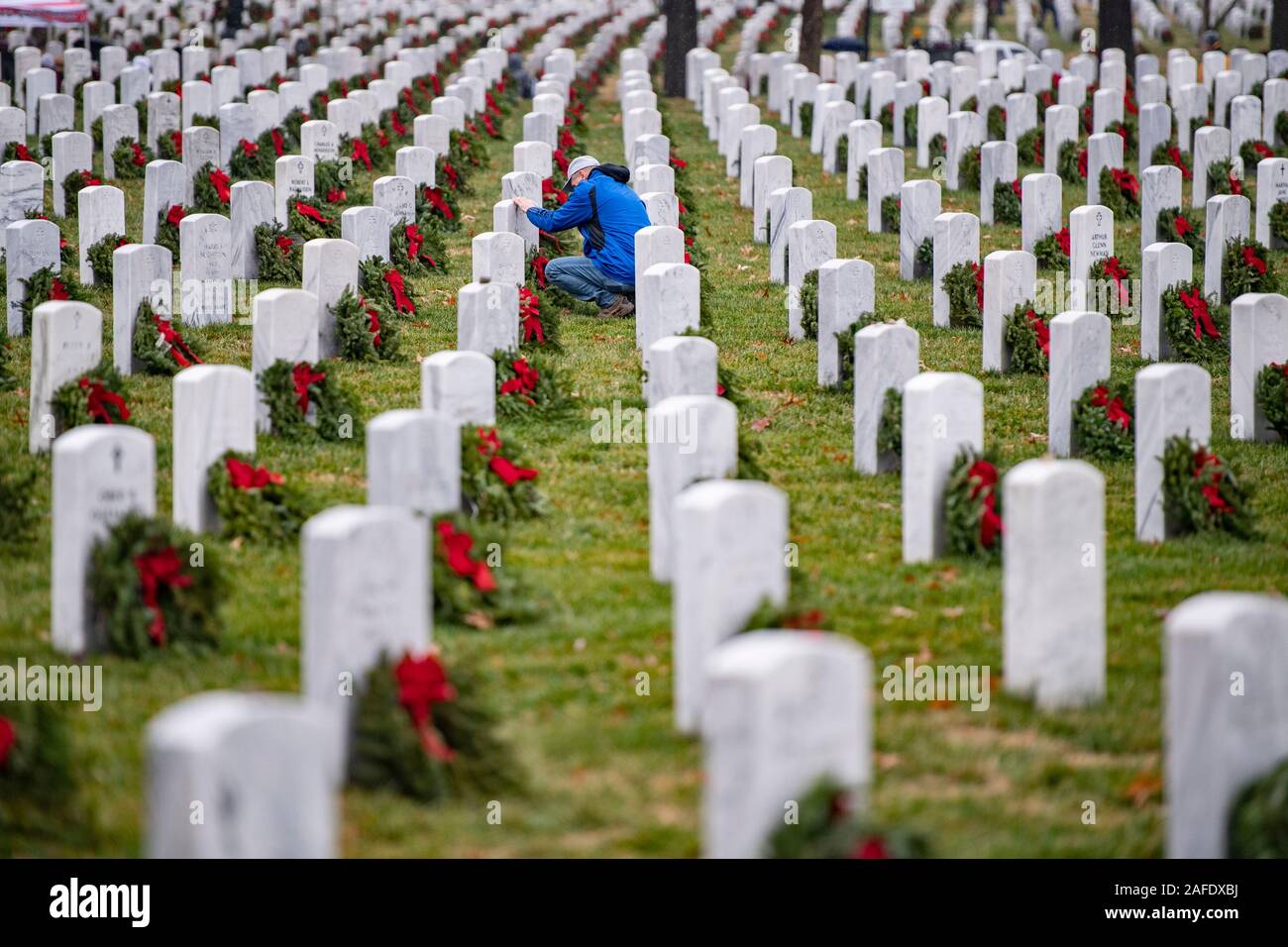 Arlington, United States of America. 14 December, 2019. A man pauses at a gravesite of a fallen service member during the 28th Wreaths Across America Day at Arlington National Cemetery December 14, 2019 in Arlington, Virginia. More than 38,000 volunteers place wreaths at every gravesite at Arlington National Cemetery and other sites around the nation.  Credit: Elizabeth Fraser/DOD/Alamy Live News Stock Photo