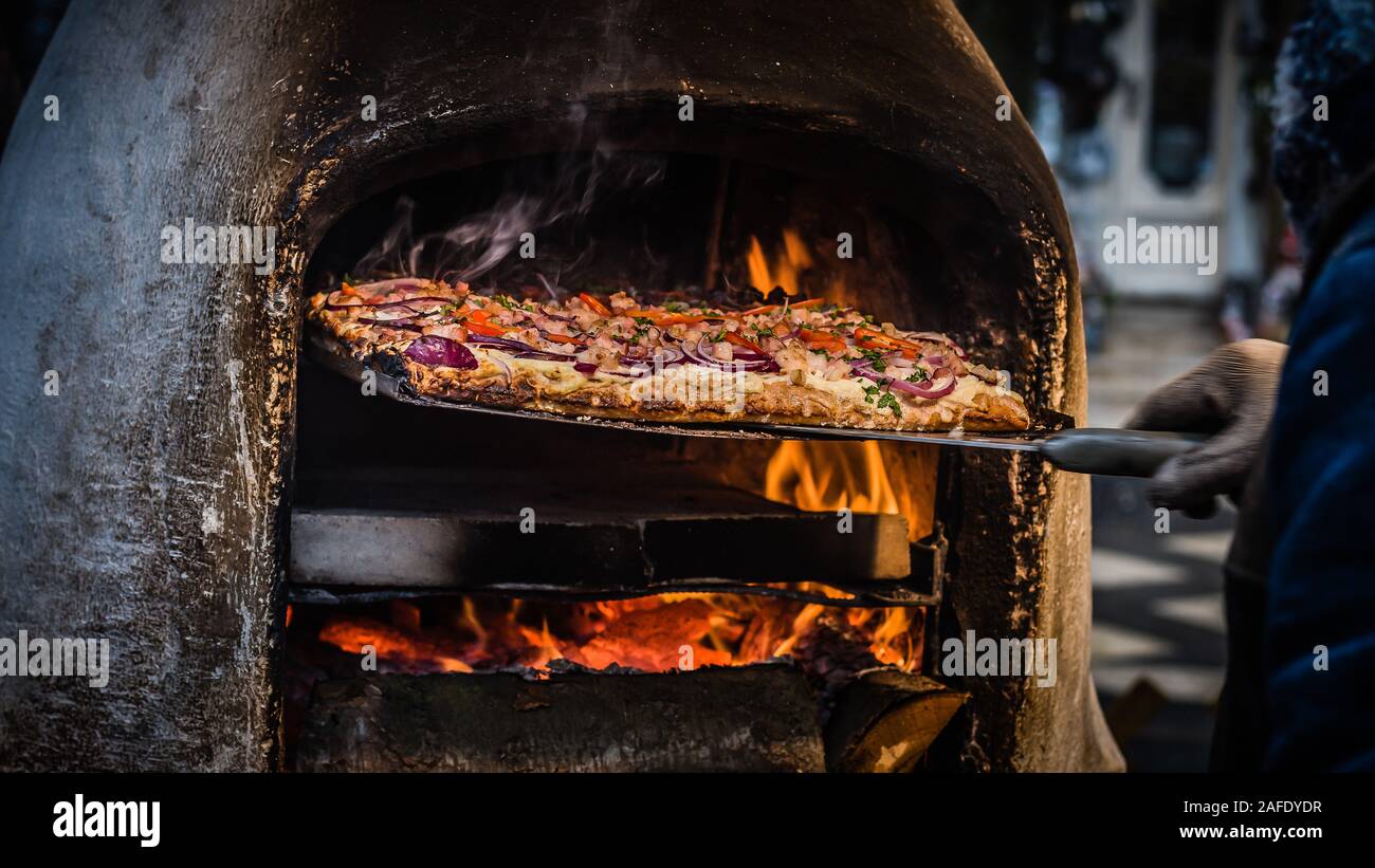 Man removing freshly made pizza street food from wood fired oven in Budapest Stock Photo