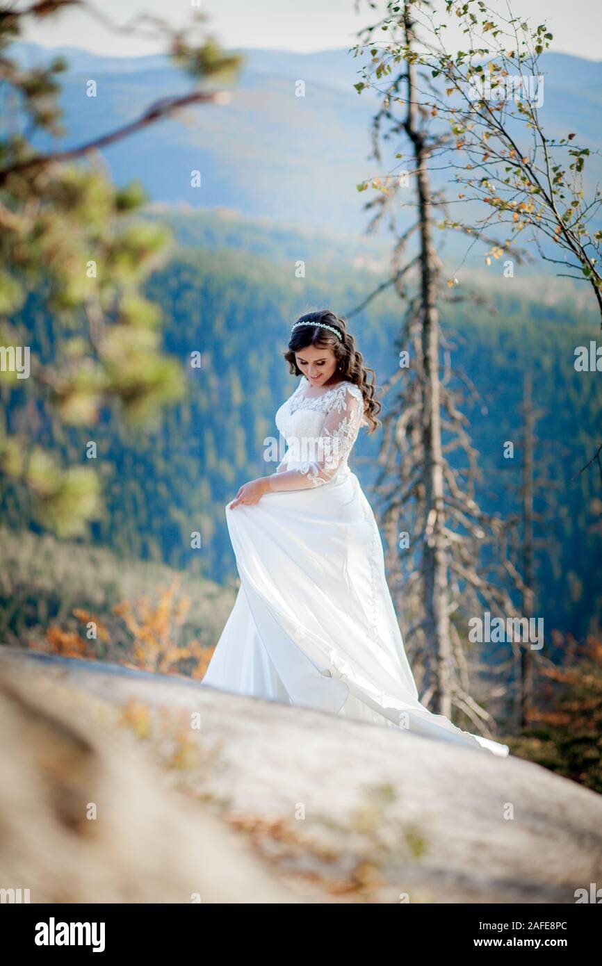 Back Of Girl In Wedding Dress Sitting On Rocks In Mountains And