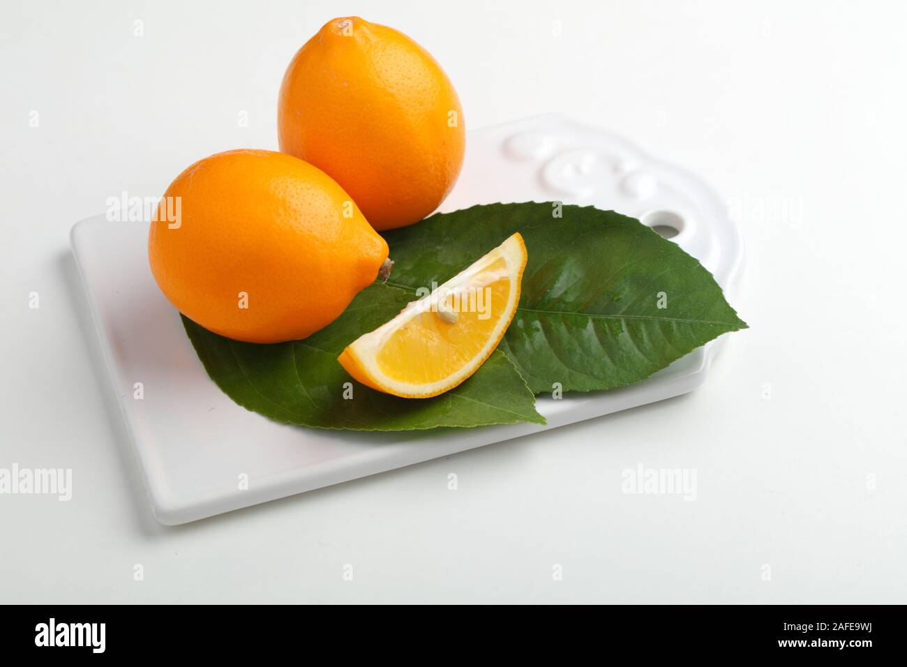 Orange colored lemon fruits with green leaves on a white cutting board Stock Photo
