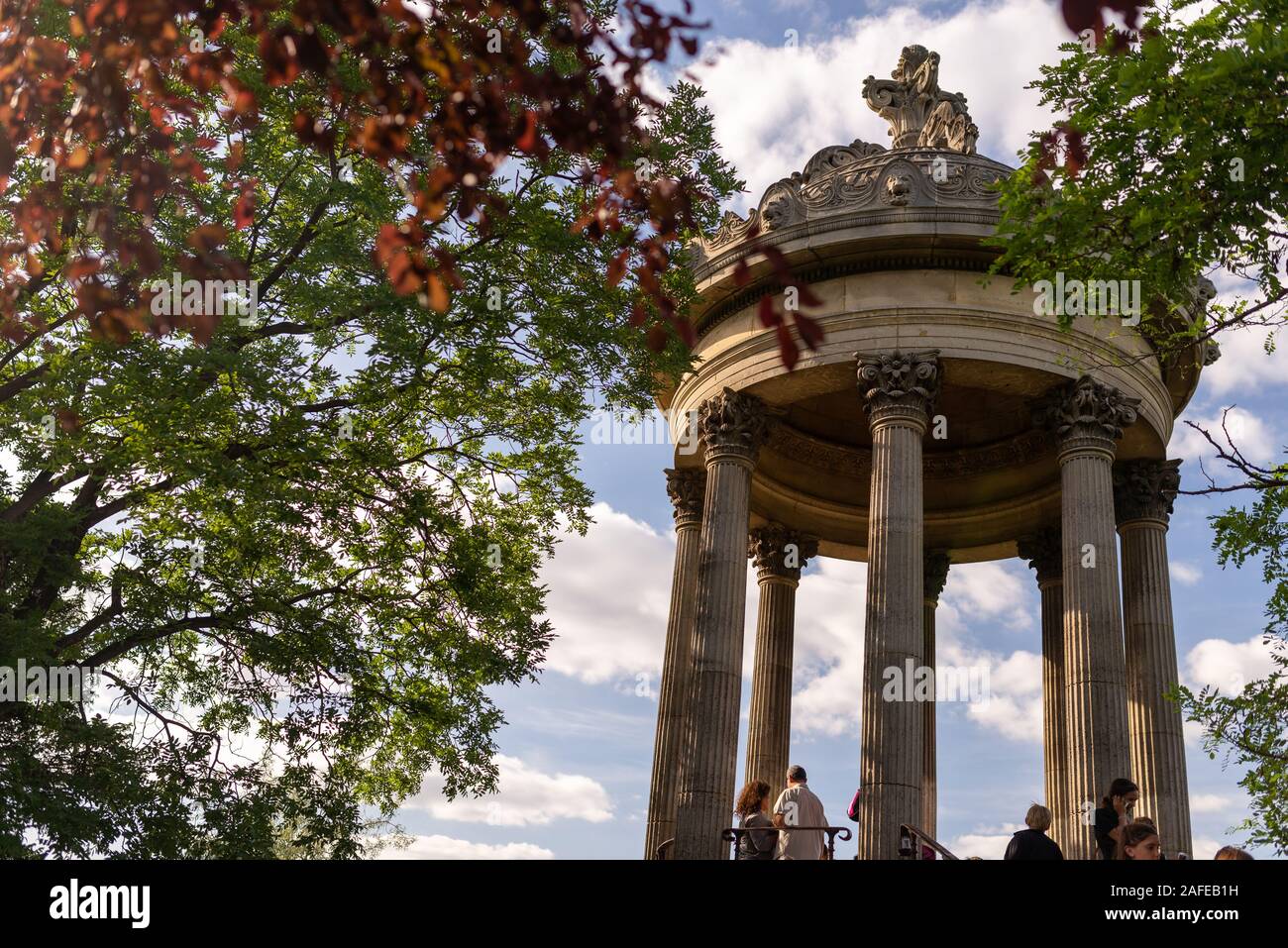 Paris, France - June 16, 2017: Visitors at the temple of the Sybil in Buttes Chaumont Park seen through tree branches, taken on a early summer sunny a Stock Photo