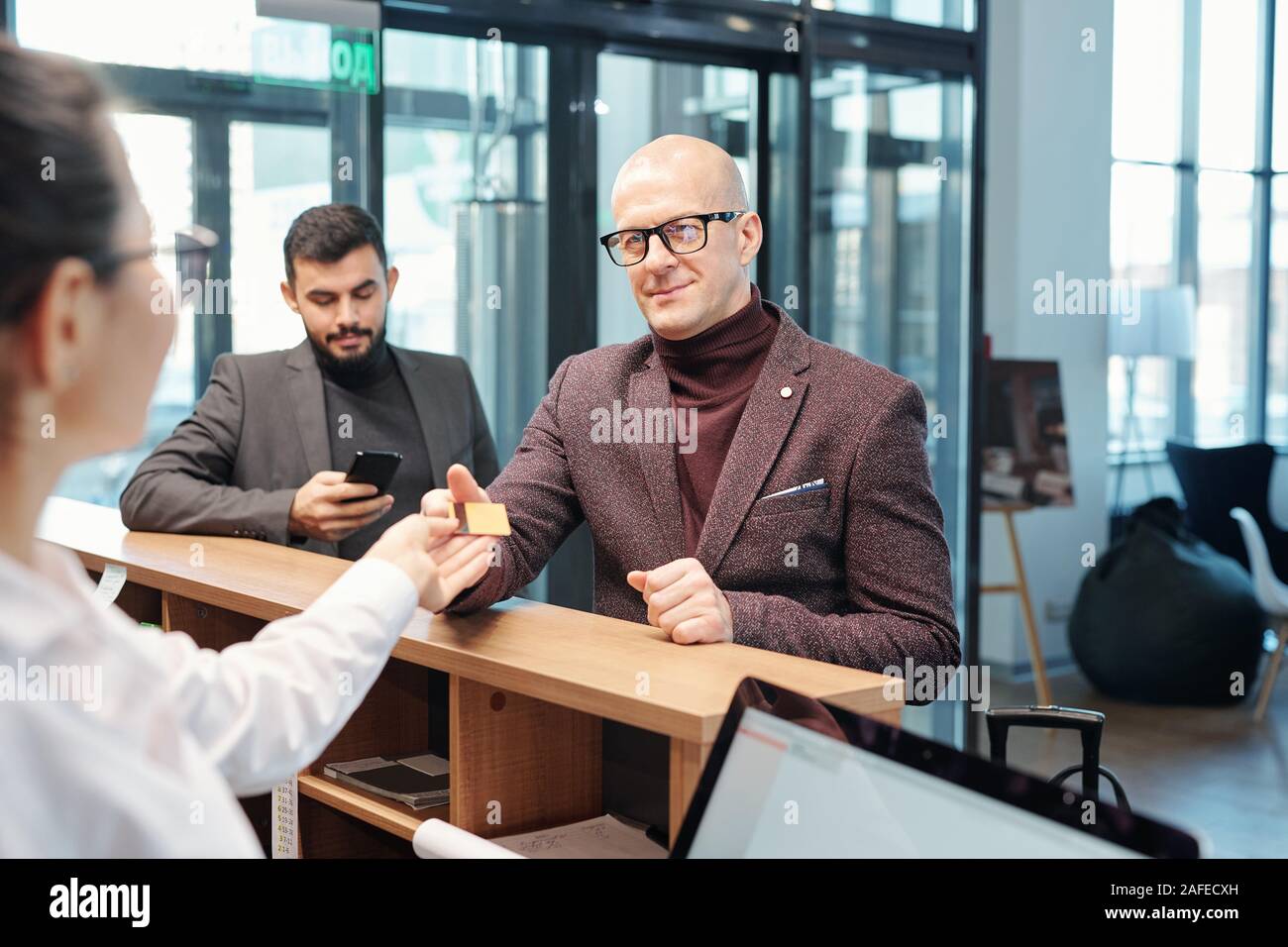 Business traveler in formalwear passing plastic card to hotel receptionist Stock Photo