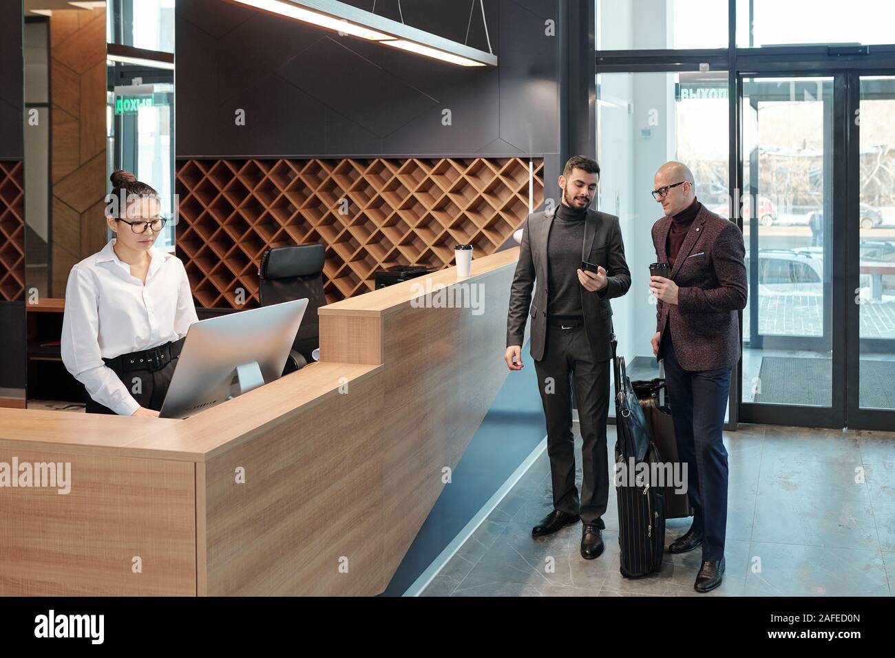 Businessmen discussing data in smartphone while receptionist using computer Stock Photo