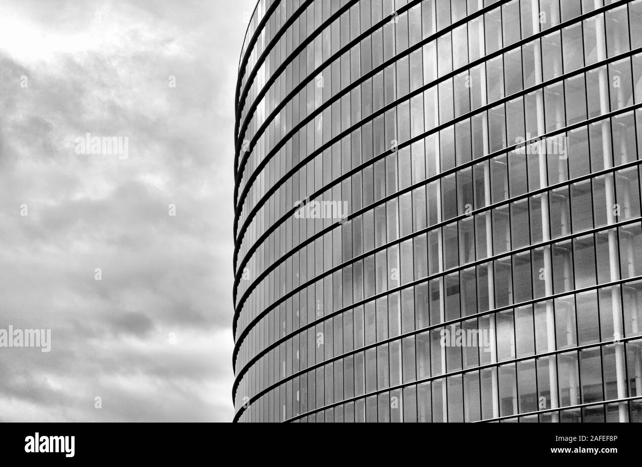 Horizontal view of a modern steel and glass building with many windows and levels and an expressive overcast sky background in black and white Stock Photo