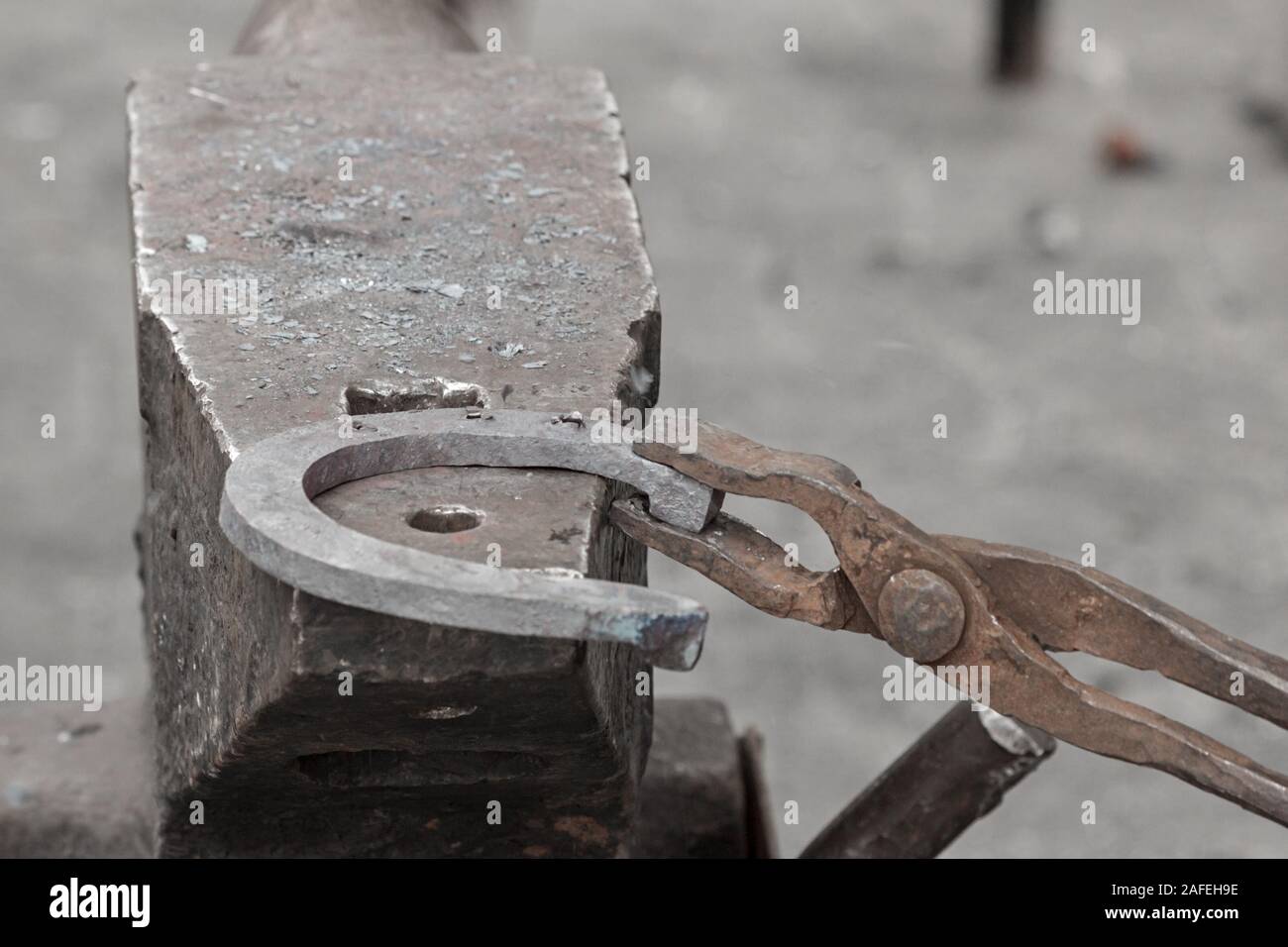 The blacksmith hold an iron horseshoe with a tongs, forging on the anvil. Stock Photo