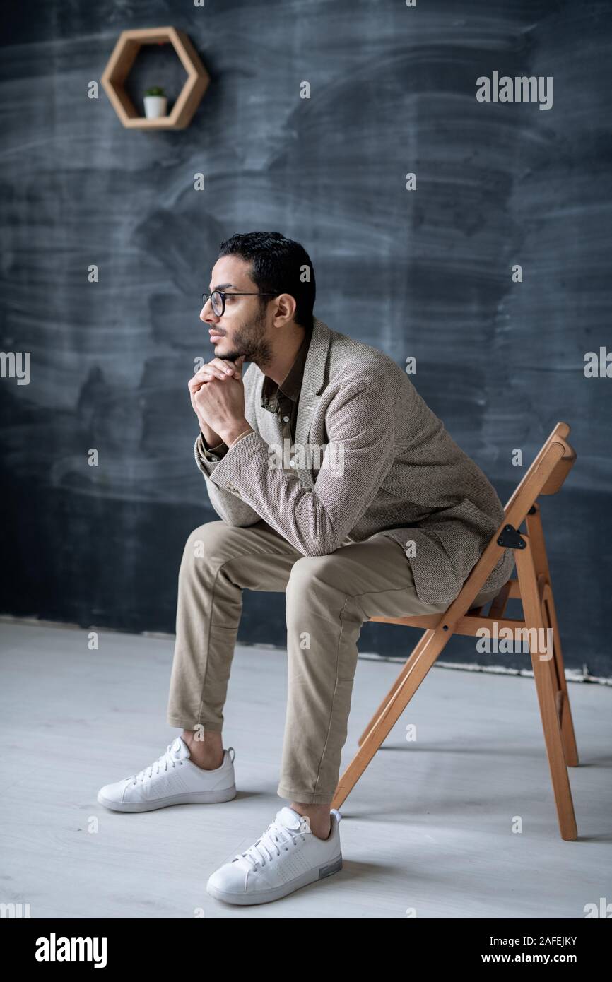 Young pensive businessman in smart casual sitting on chair in front of camera Stock Photo