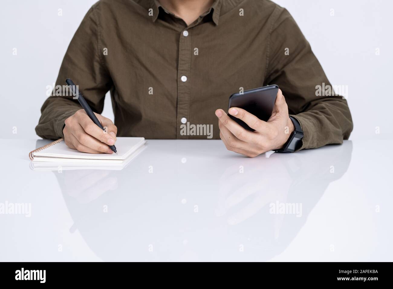 Hands of young businessman with smartphone and pen writing down working plan Stock Photo
