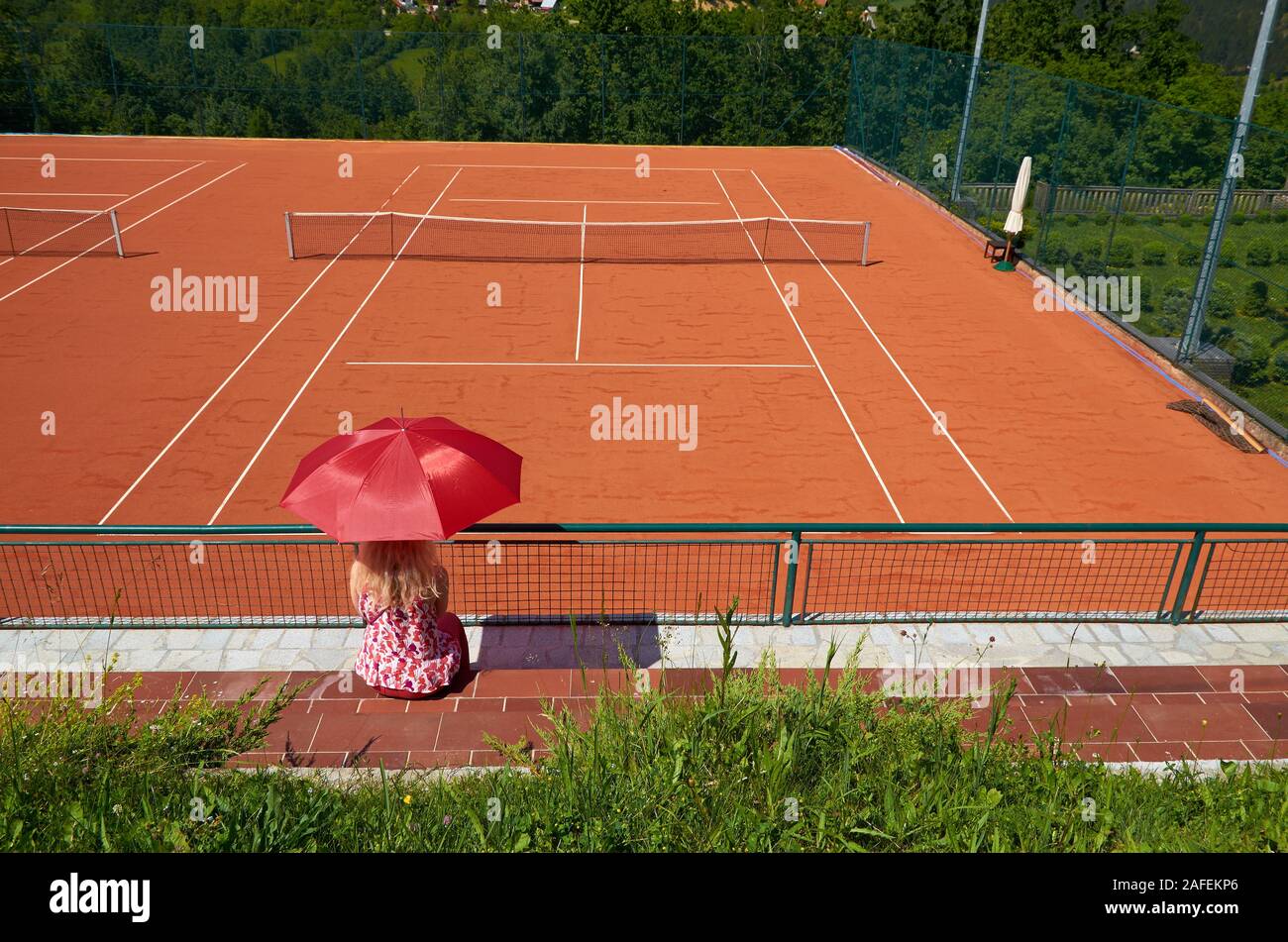 Woman with an umbrella for sun protection watching an empty tennis