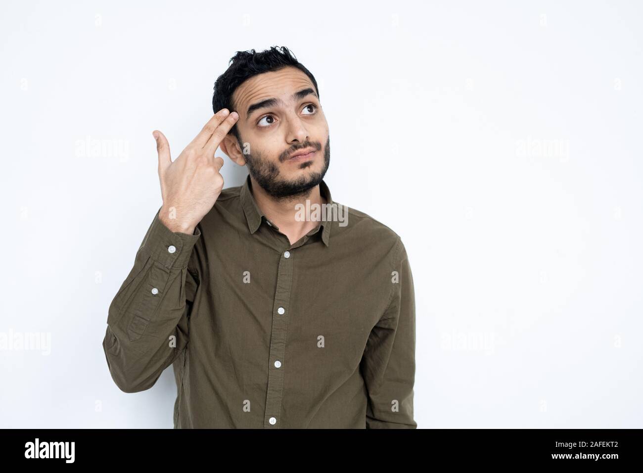 Perplexed young man in casualwear holding two fingers by his head Stock Photo