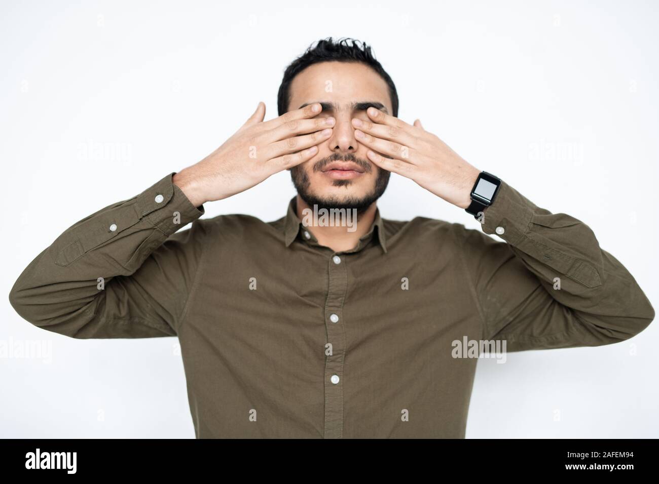 Young tired man in shirt covering his eyes by hands at break between work Stock Photo