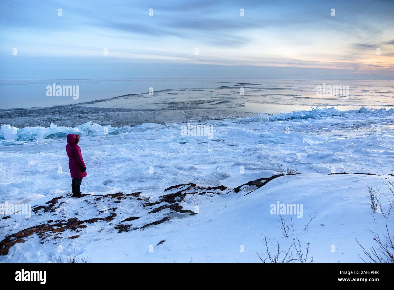 A person wearing a parka coat watching a cold winter sunset along the North Shore of Lake Superior, Minnesota Stock Photo