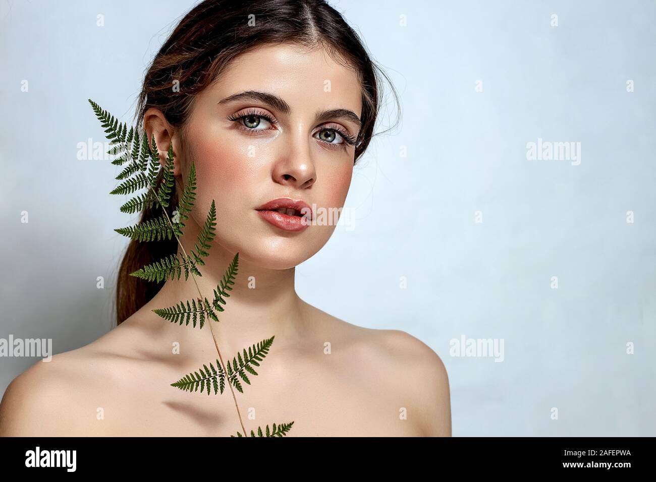 Portrait of an adult brunette woman on a white background with green fern, skin care concept, beautiful skin and hands with nail manicure. Stock Photo