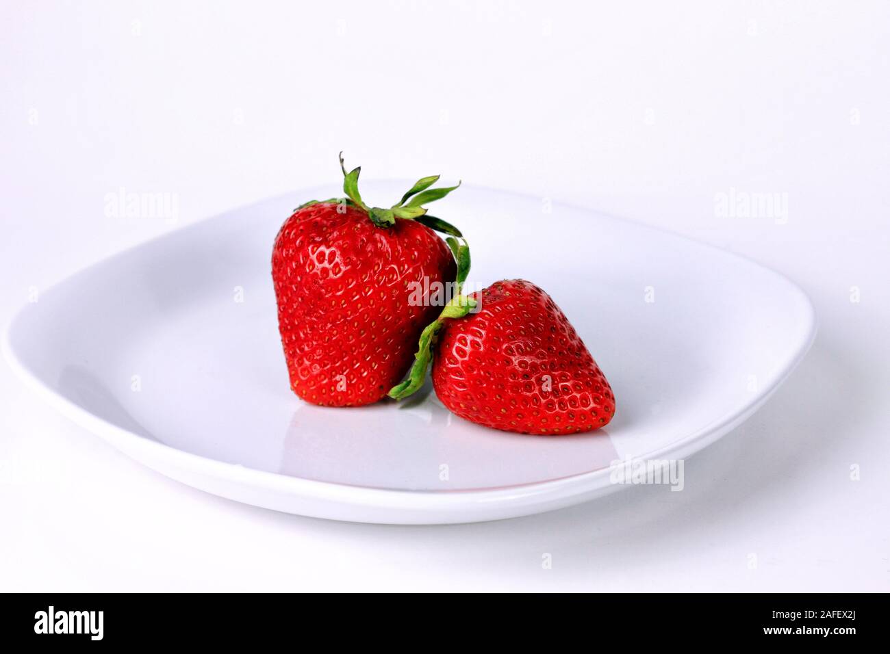 Two ripe red strawberries on a white plate against a white background. Stock Photo