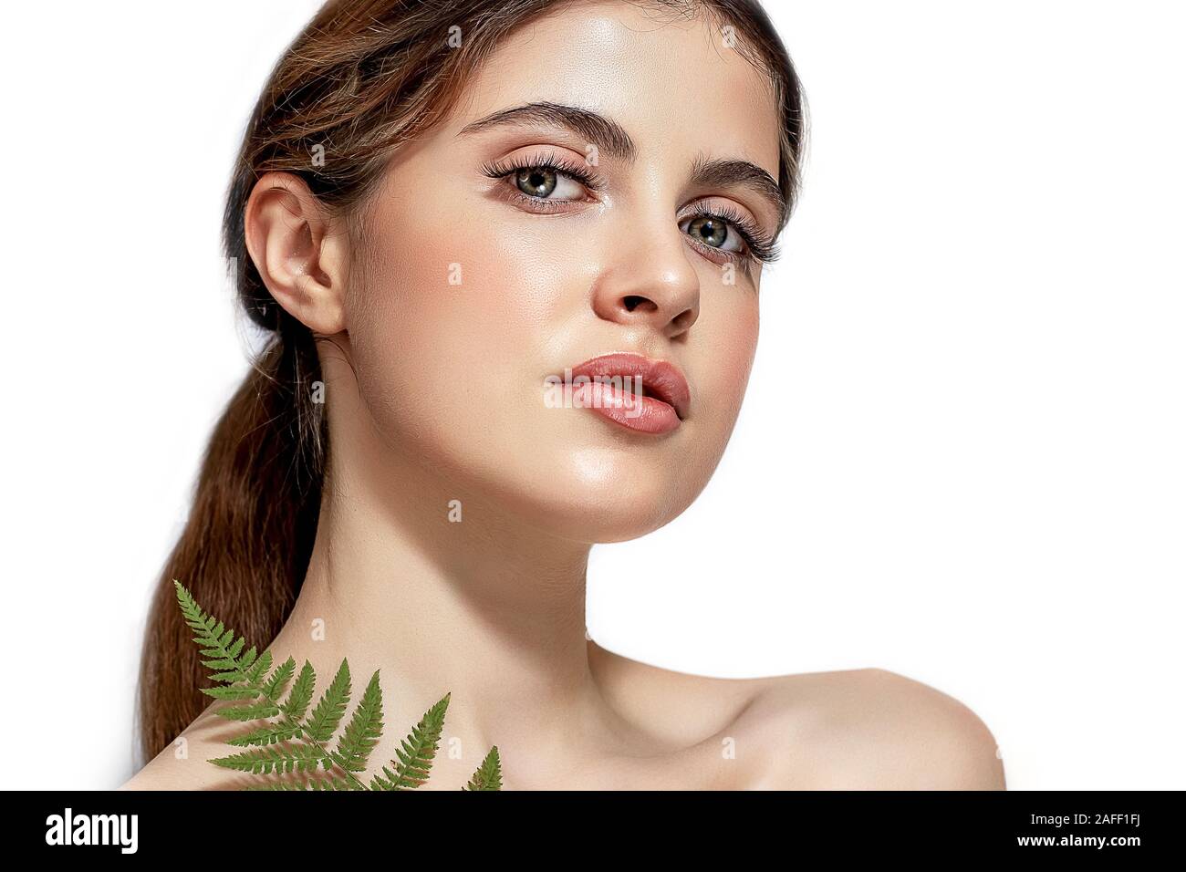 Portrait of an adult brunette woman on a white background with green fern, skin care concept, beautiful skin and hands with nail manicure. Stock Photo