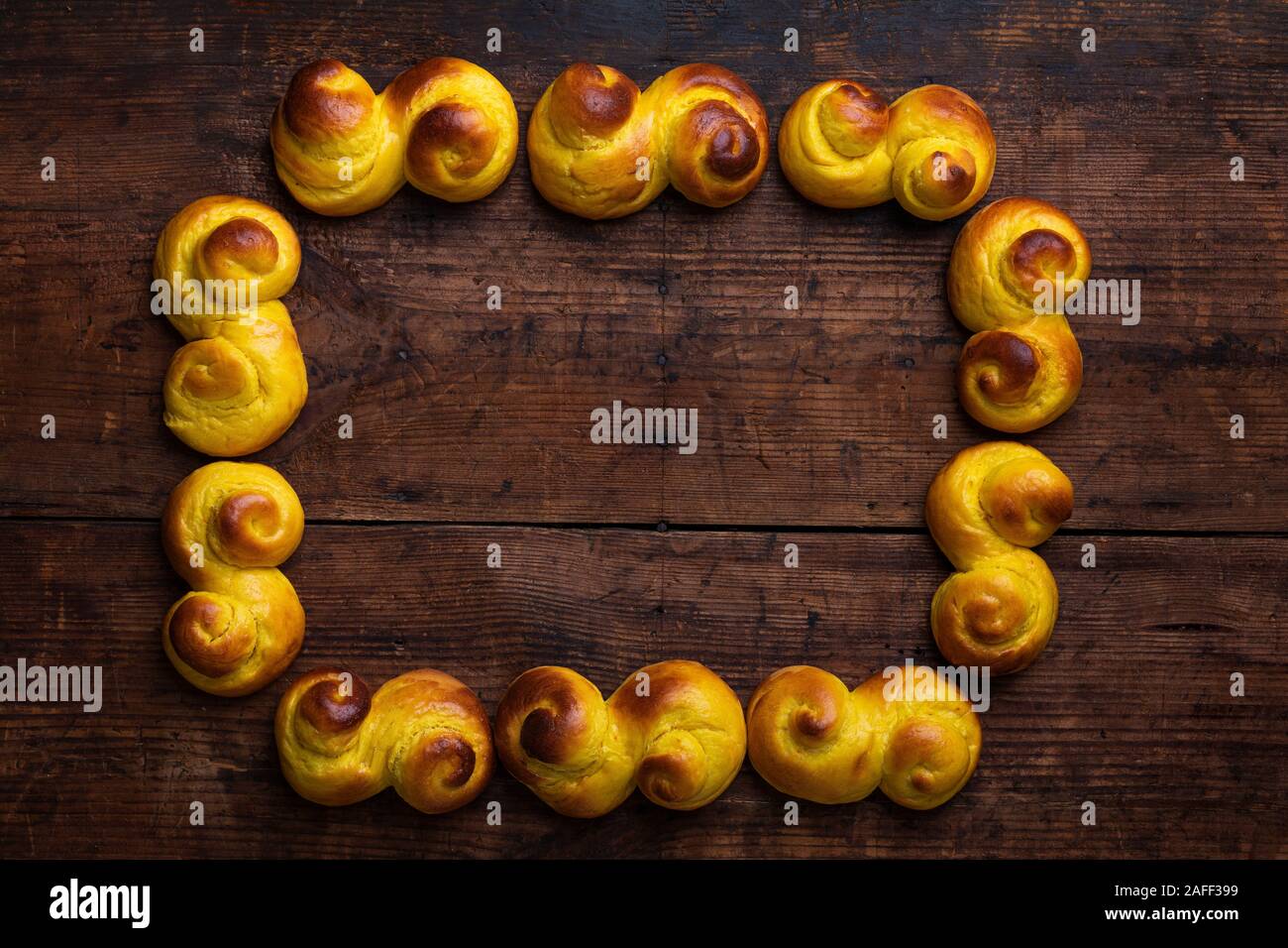 Swedish traditional christmas bun Lussekatter or Lussebullar on a rustic wooden table, in the shape of a frame with copy space. The buns are freshly m Stock Photo