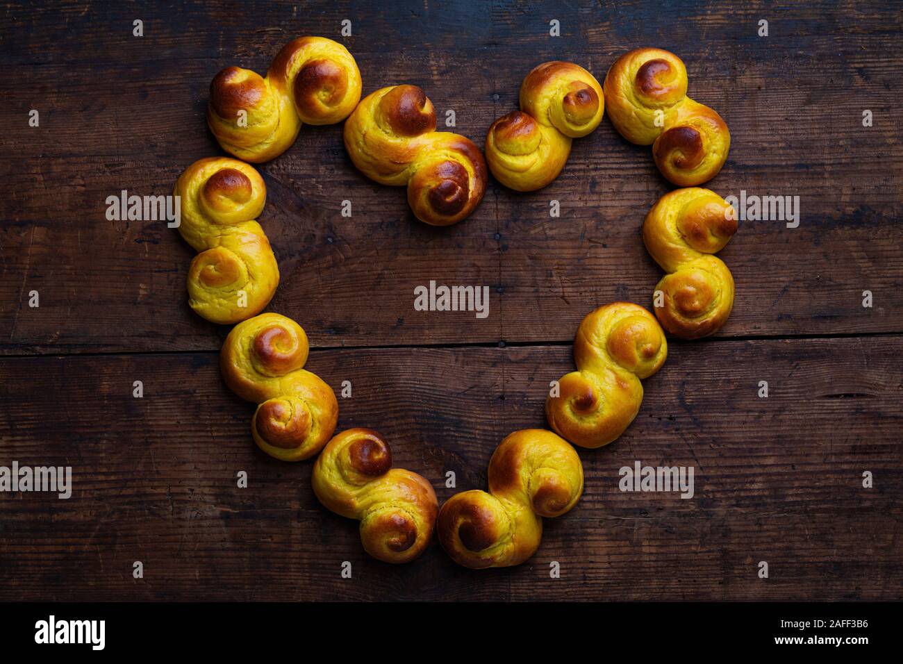 Swedish traditional christmas bun Lussekatter or Lussebullar on a rustic wooden table, in the shape of a heart. The buns are freshly made and homemade Stock Photo
