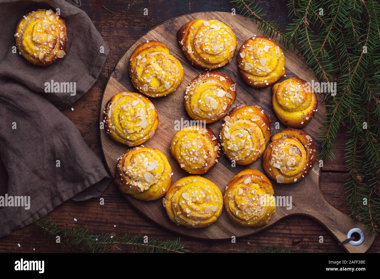Freshly baked homemade Swedish traditional saffron buns, also known as lussebullar or saffransbröd. Seen from above flat lay on a dark wooden table su Stock Photo